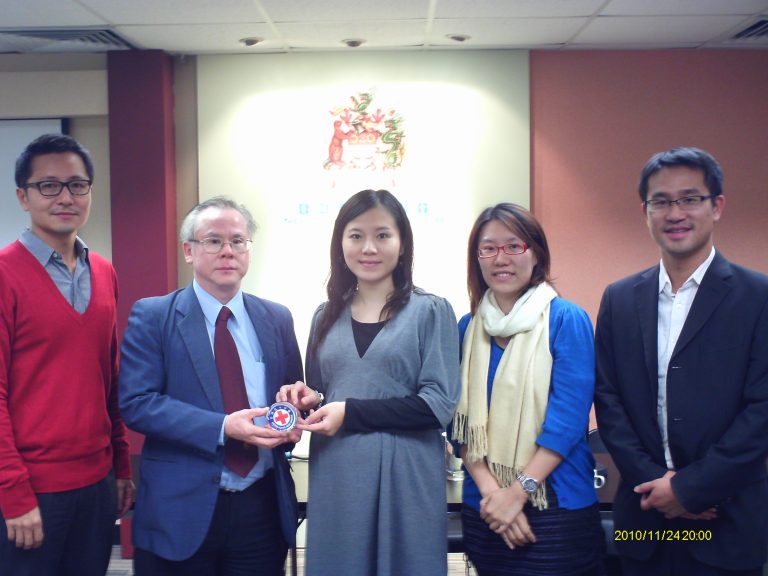 Five people in an office setting, two exchanging a Red Cross emblem.