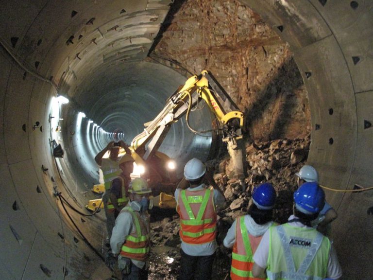 Construction workers operate excavator inside tunnel under construction