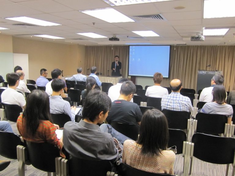Audience attending a presentation in a conference room with a speaker at the front.