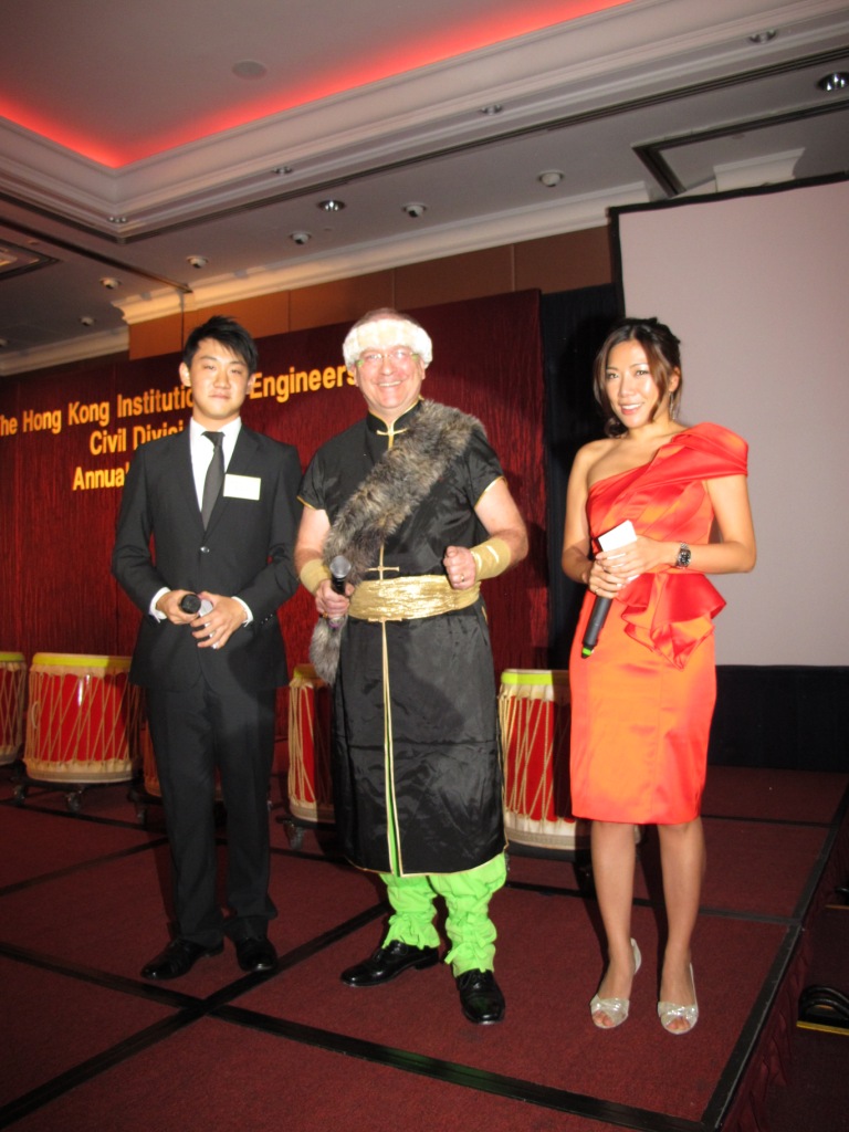 Three people posing on stage at an event, one in formal wear, one in costume, one in a red dress.