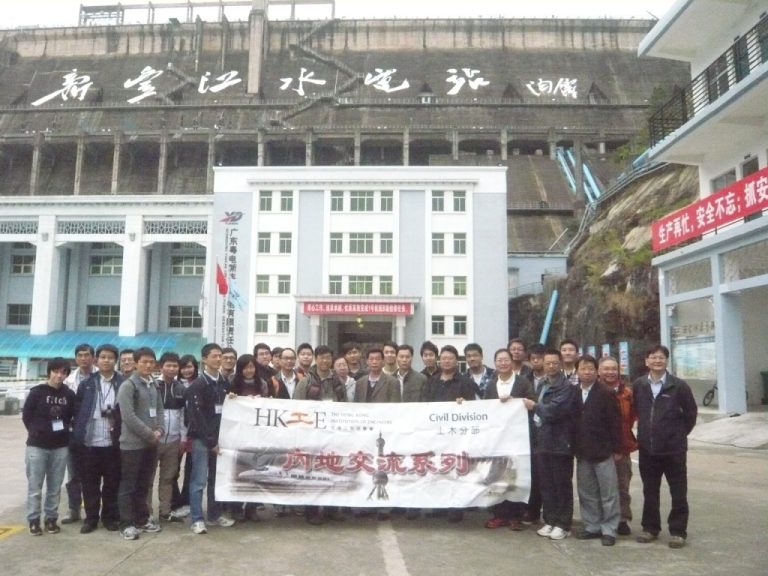 Group of engineers posing with banner in front of a large dam structure.