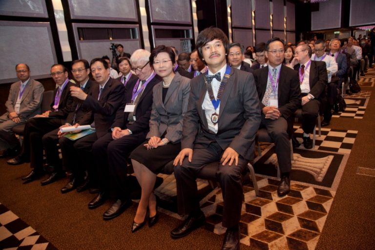 Audience at formal event seated in rows, attentive and dressed in business attire.