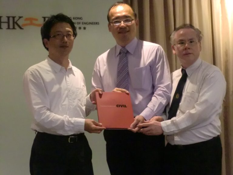 "Three men in business attire presenting a red folder labeled ""CIVIL"" at an event."