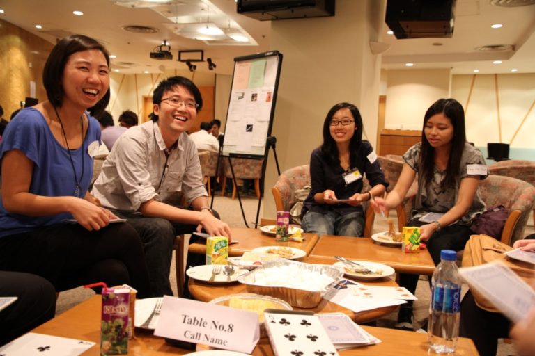 Group of people smiling and socializing at a conference table with food and drinks.
