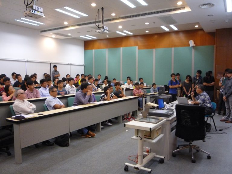 Audience in lecture hall listening to presentation with projector and laptop visible