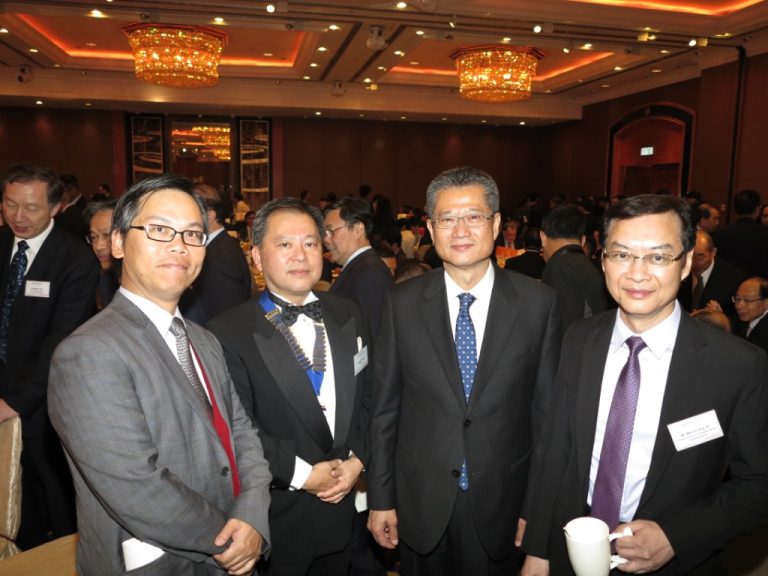 Four men in formal attire posing together at a well-lit indoor event.
