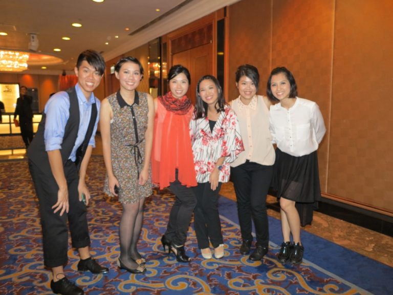Six people smiling for a photo in a hotel hallway with patterned carpet.