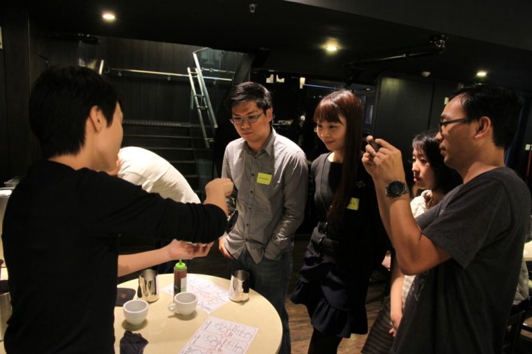 Group of people gathered around table, one pouring liquid into cup.