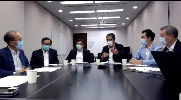 Five men in business attire and face masks seated around a conference table during a meeting.