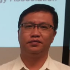 Man wearing glasses and light-colored shirt, standing in front of presentation screen