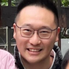 Smiling man with glasses wearing a pink shirt and dark jacket