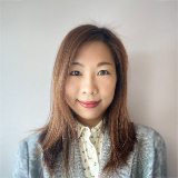 Portrait of a woman with long brown hair wearing a patterned blouse and light jacket.