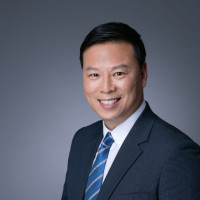 Professional headshot of Ir-Kelvin-Tang in suit and tie, smiling against gray background