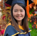 Graduate in cap and gown smiling outdoors during autumn