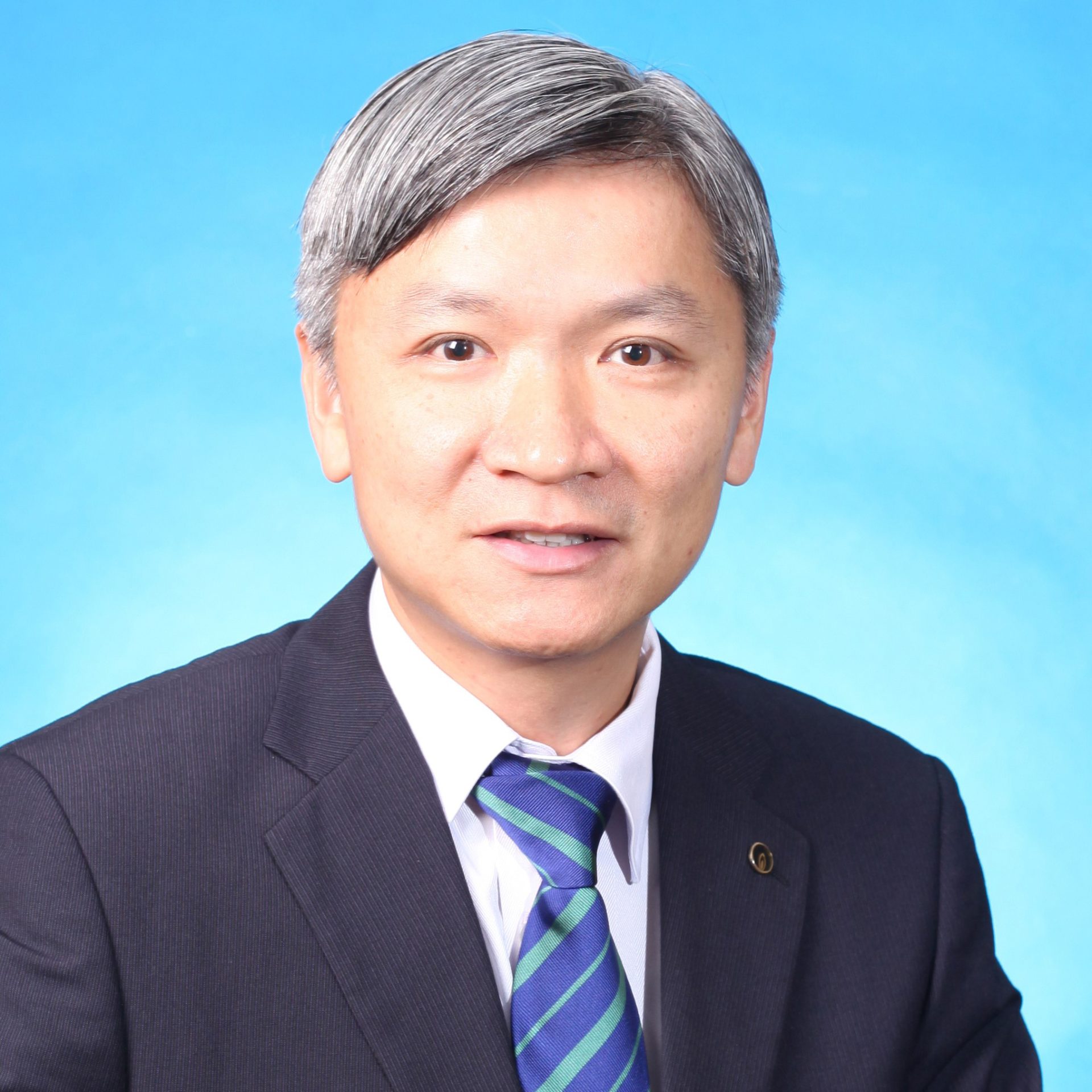 Portrait of a man with gray hair wearing a suit and striped tie against a blue background.