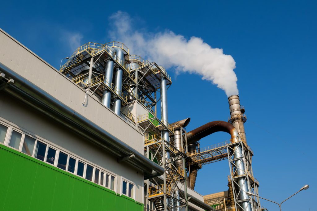 Industrial plant emitting smoke from tall chimney against clear blue sky