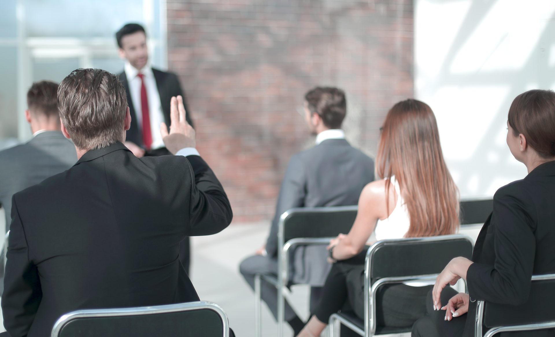 Attendee raises hand to ask question during business conference presentation.