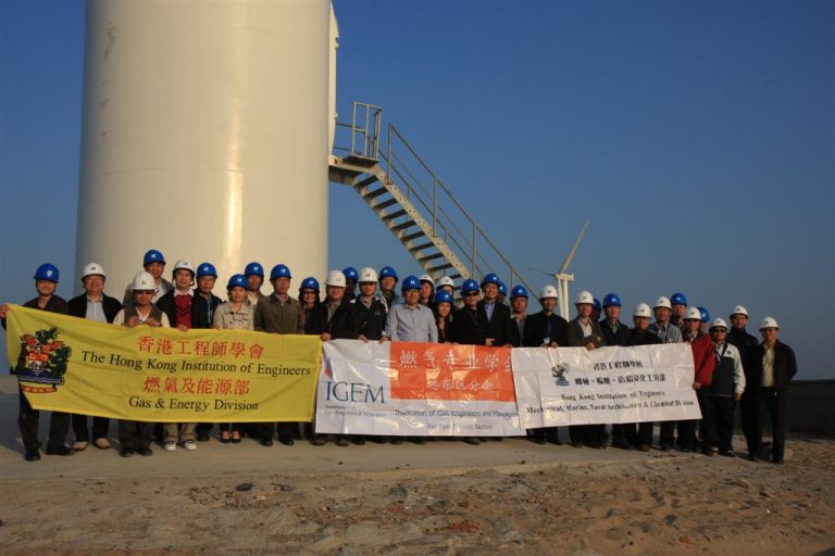 Engineers in hard hats pose with banners at a wind turbine site.
