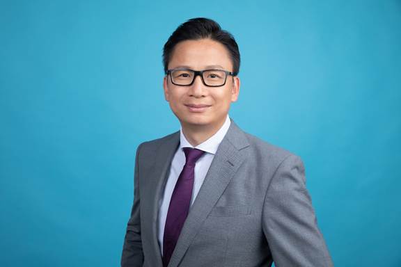 Portrait of a man in a suit and glasses against a blue background.
