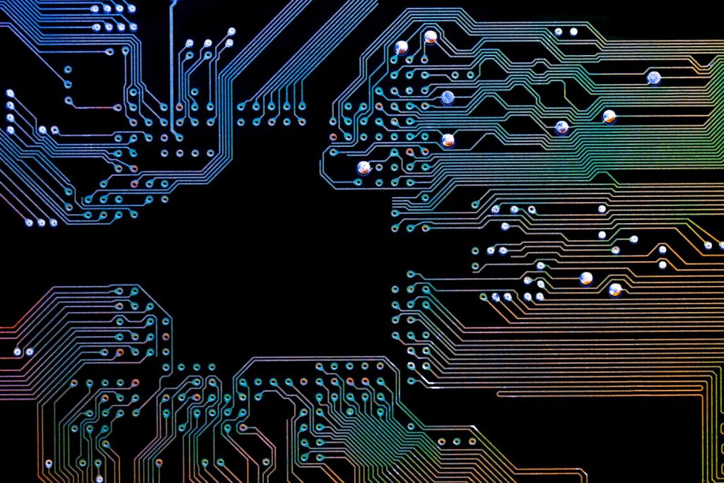 Illuminated circuit board with glowing blue, green, and orange pathways against a black background.