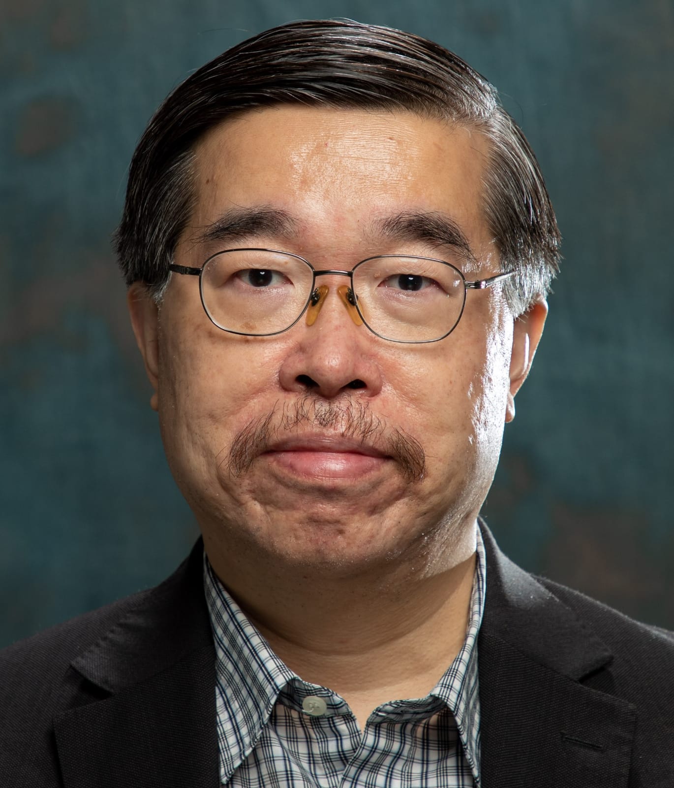 Portrait of a man with glasses and mustache wearing a suit and plaid shirt.