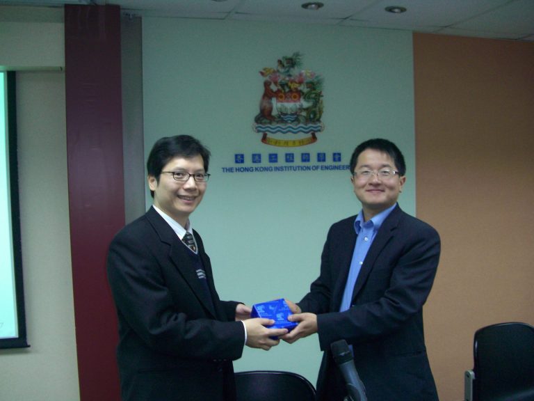 Two men in suits exchange a blue gift box at The Hong Kong Institution of Engineers.