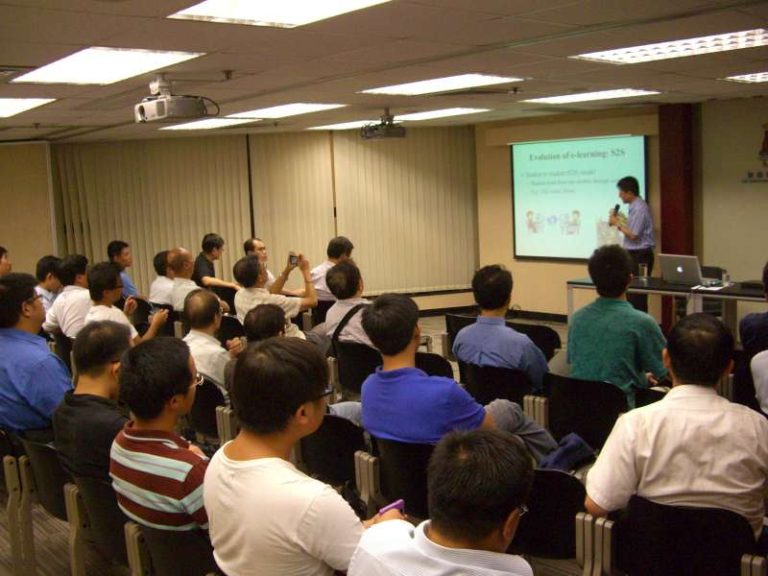 Audience attending e-learning seminar with presenter at front and projection screen
