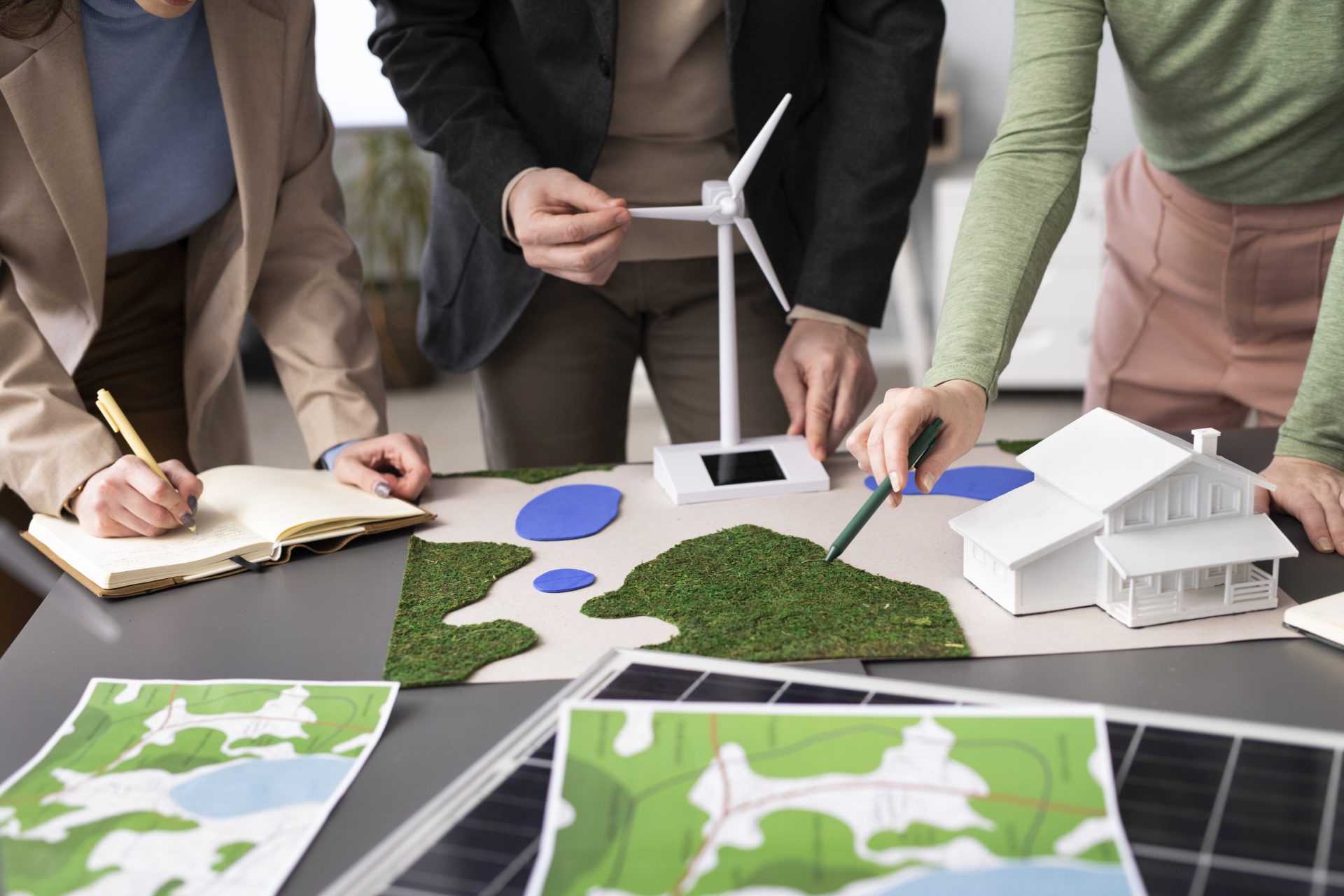 Researchers planning renewable energy solutions with wind turbine, solar panels, and house model.