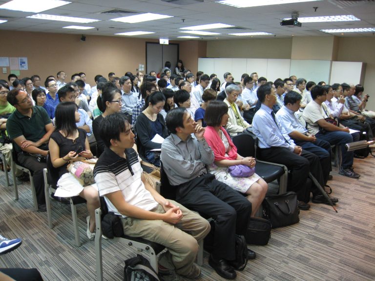 Audience seated in rows listening to presentation in conference room.
