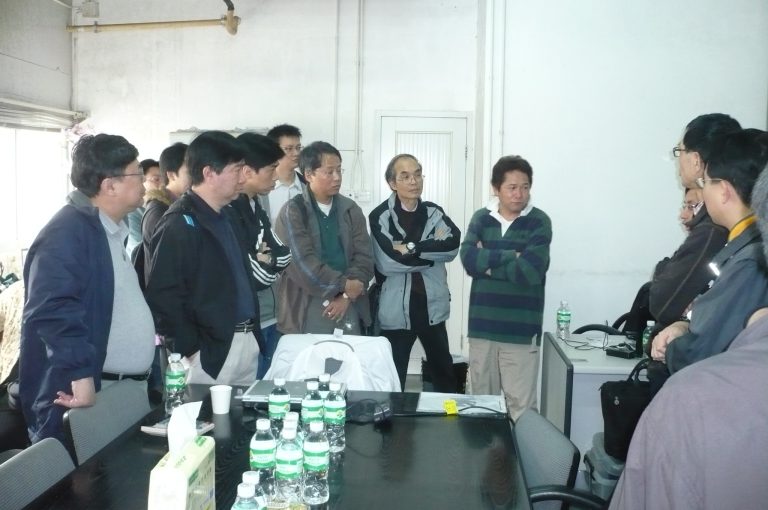 Group of men in a meeting room, some standing, some seated around a table with water bottles.