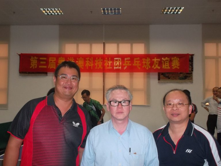 3 men at table tennis event with banner behind