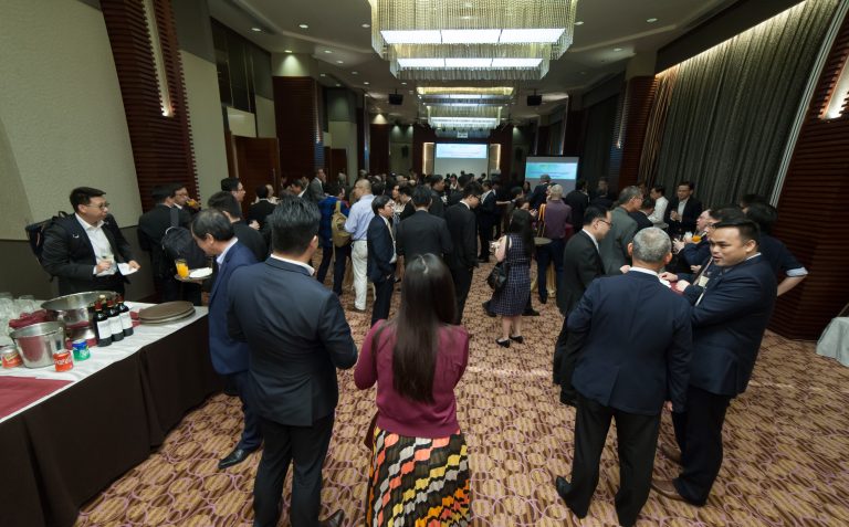 Attendees networking at a conference in a well-lit ballroom with presentation screens.
