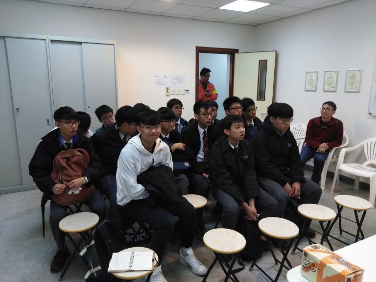 Group of students seated on stools in a classroom setting, attentively listening.