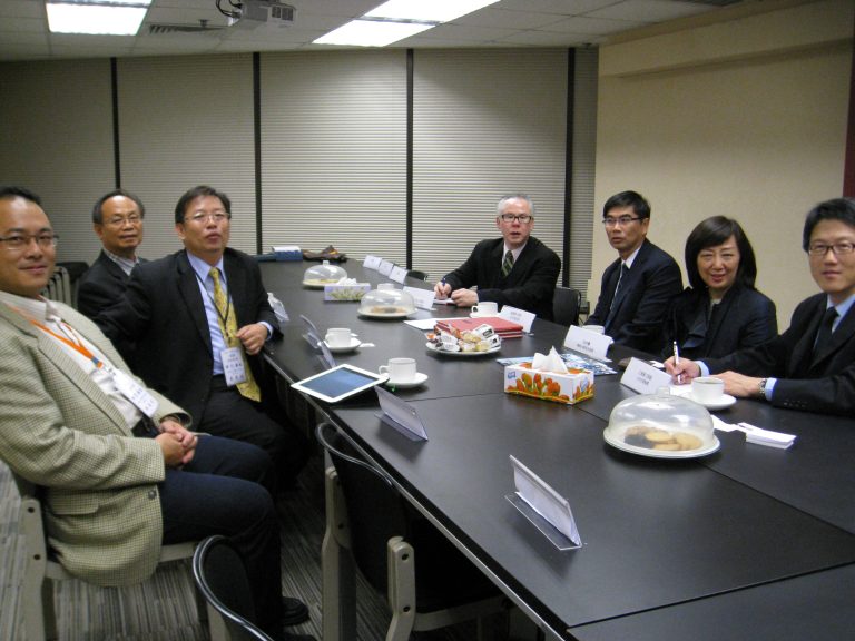 Seven professionals in business attire seated around a conference table with refreshments.