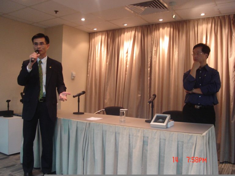 Man speaks into mic, another listens nearby