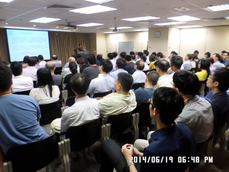 Audience attending a presentation in a conference room with a speaker at the front.