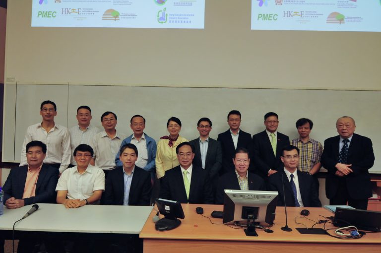Group of professionals posing for photo at event with logos displayed on screen behind them.