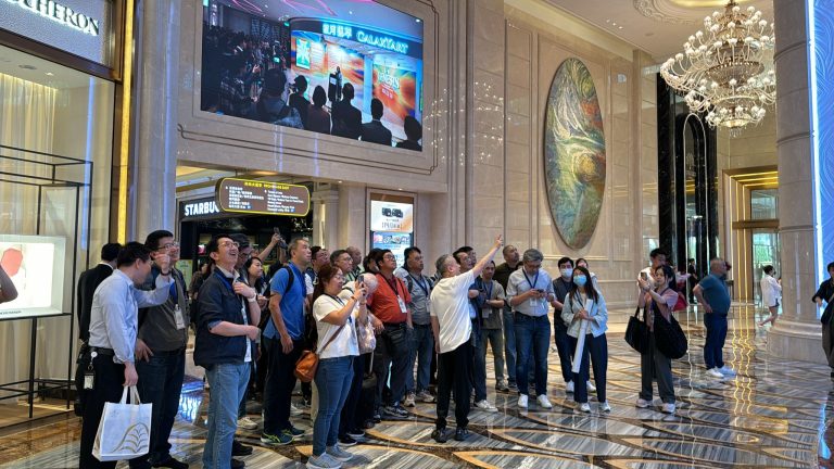 Group of people gathered in a luxury mall lobby, looking up at a large screen and artwork.
