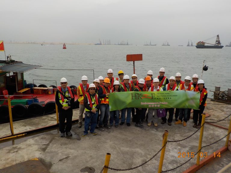 Group of engineers in safety gear holding banner at waterfront, 2015
