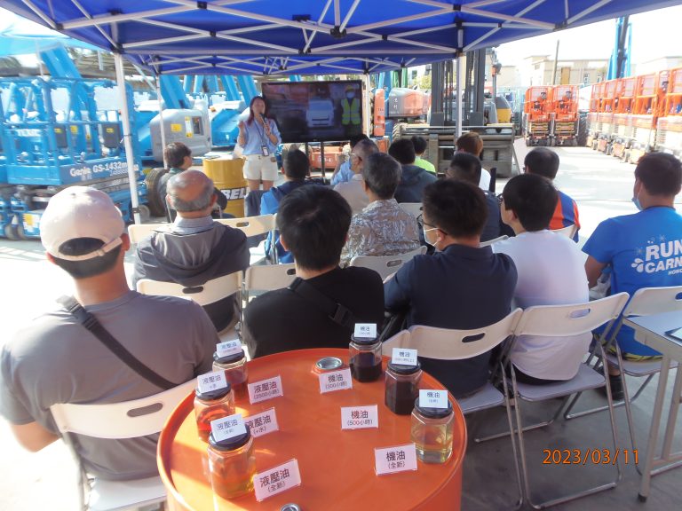 Group attending outdoor presentation under blue tent with construction equipment in background.