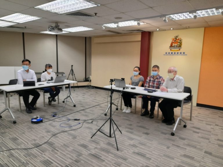 Five people wearing masks seated at tables with laptops in a conference room.