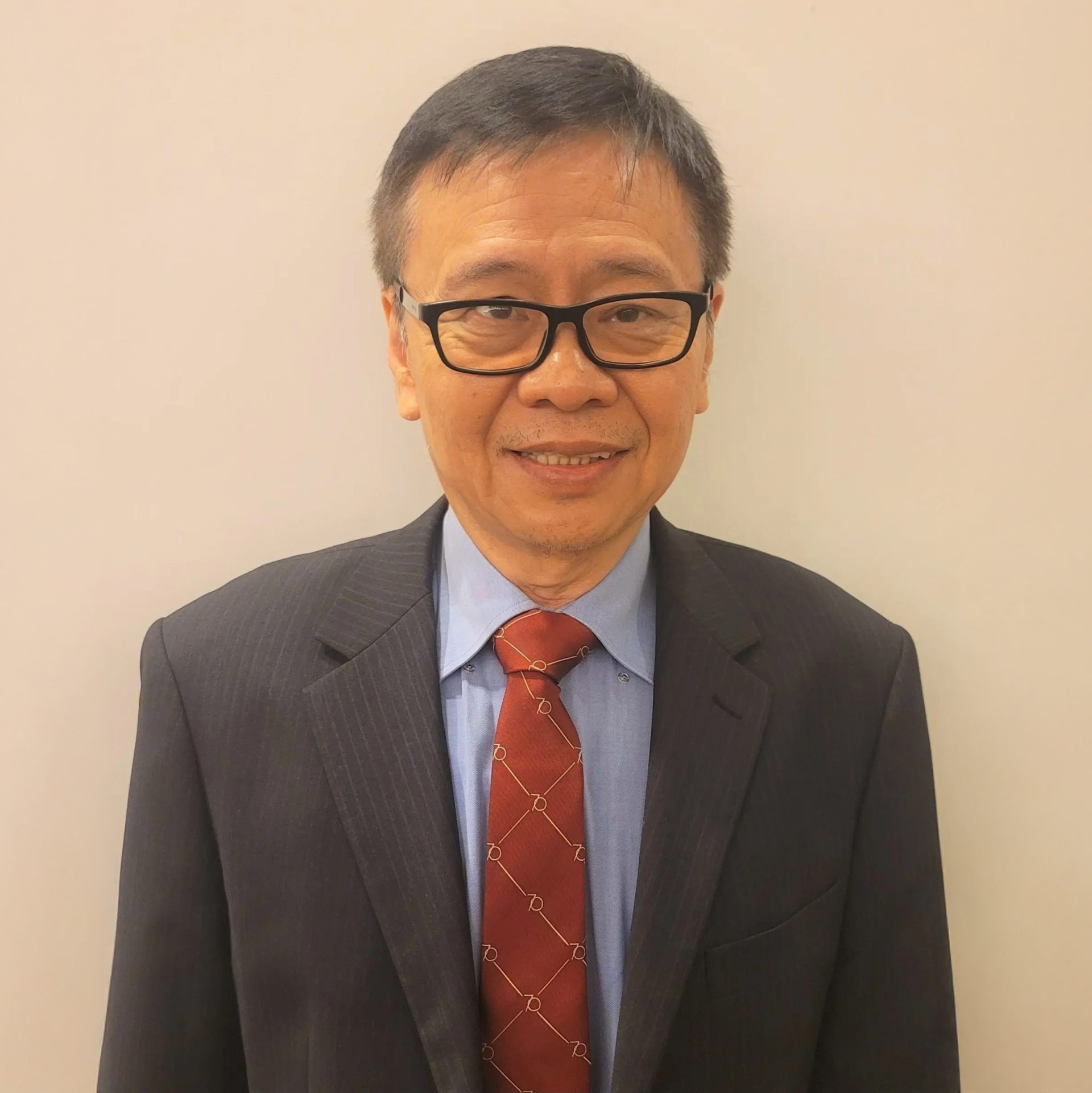 Man wearing glasses, dark suit, blue shirt, and red patterned tie.