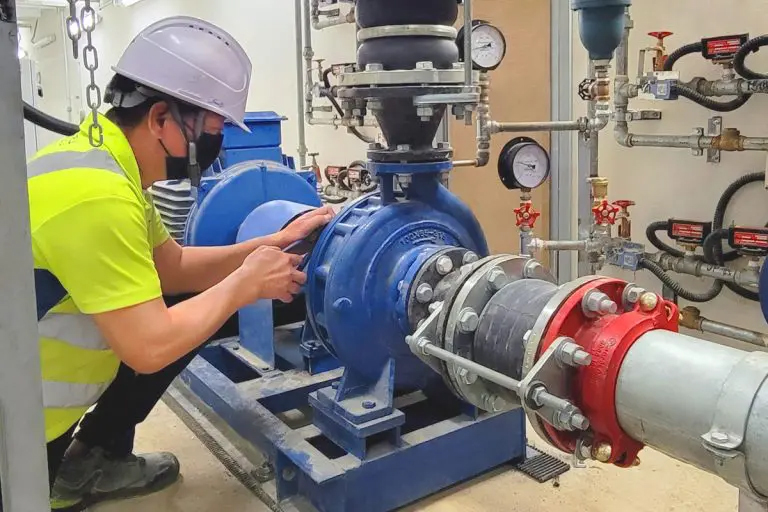Engineer in safety gear inspecting industrial pump and piping system.