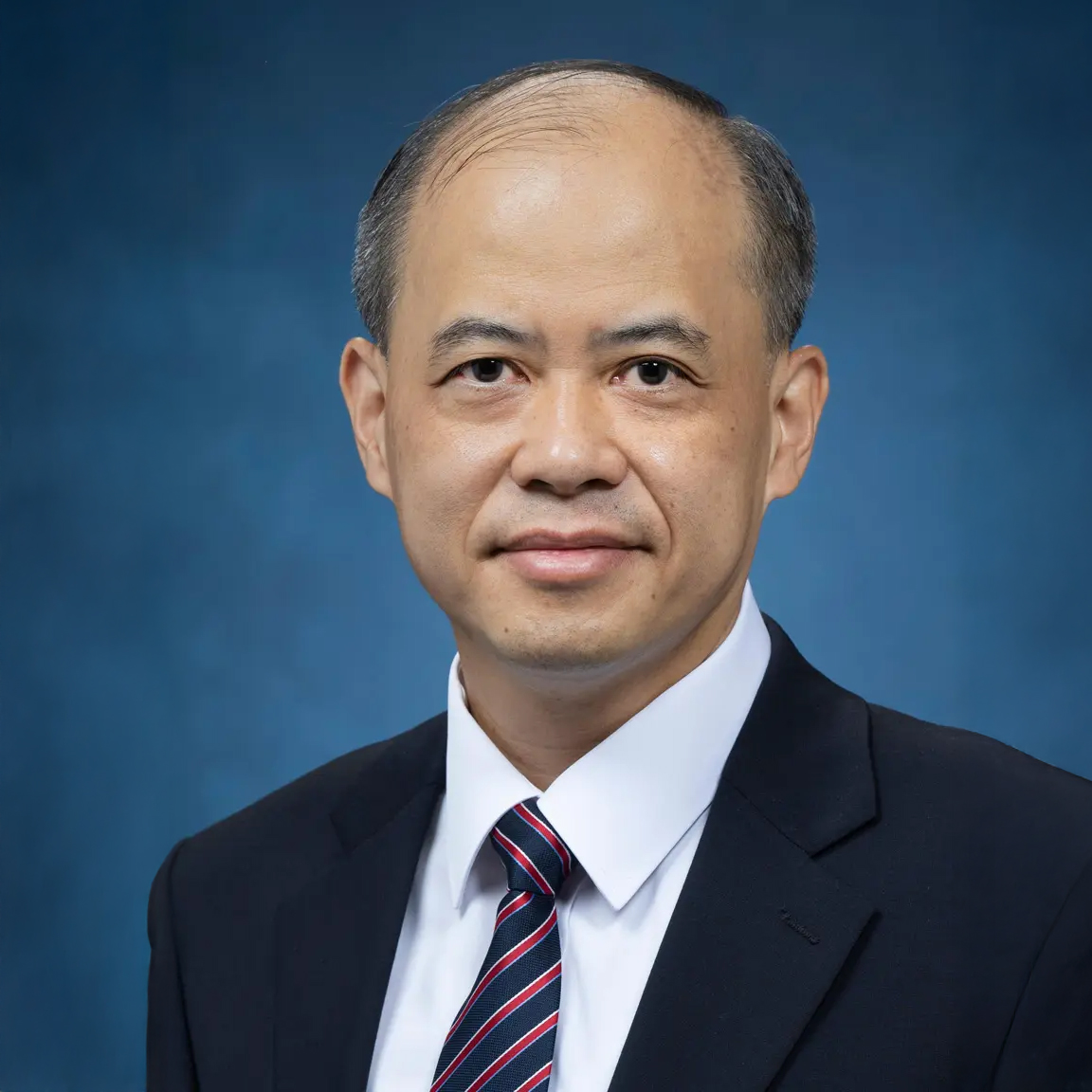 Portrait of a man in a suit and tie against a blue background.