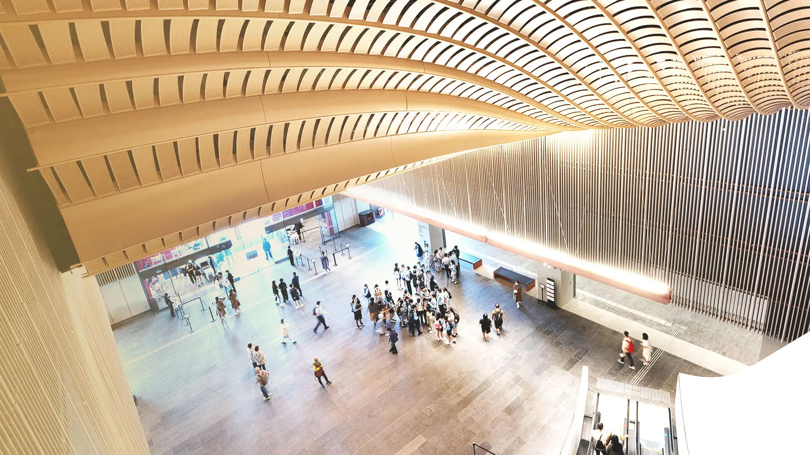 High-angle view of modern transit station with curved wooden ceiling and people moving through spacious hall.