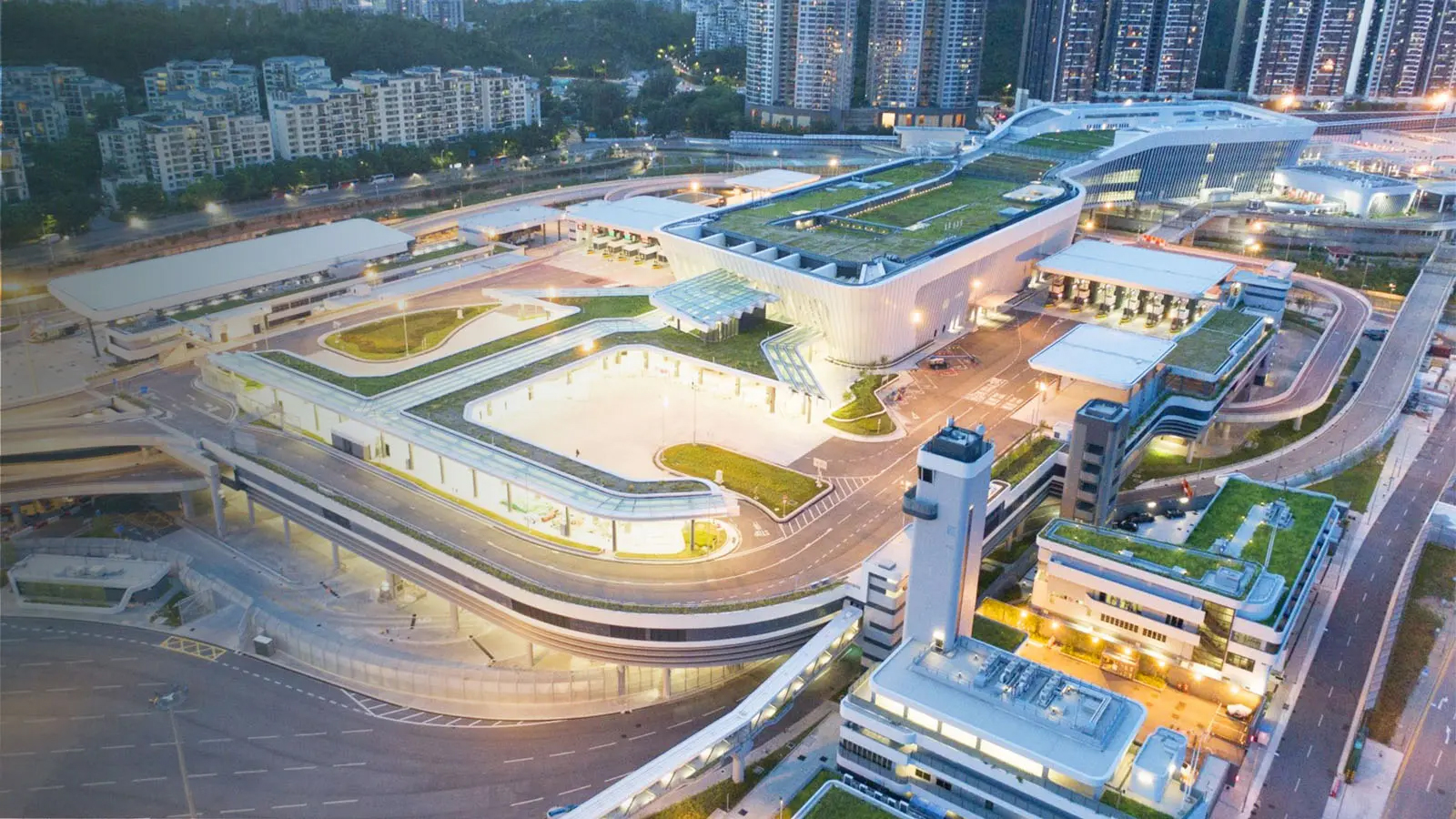 Aerial view of modern transportation hub with green roofs and surrounding urban buildings at dusk.