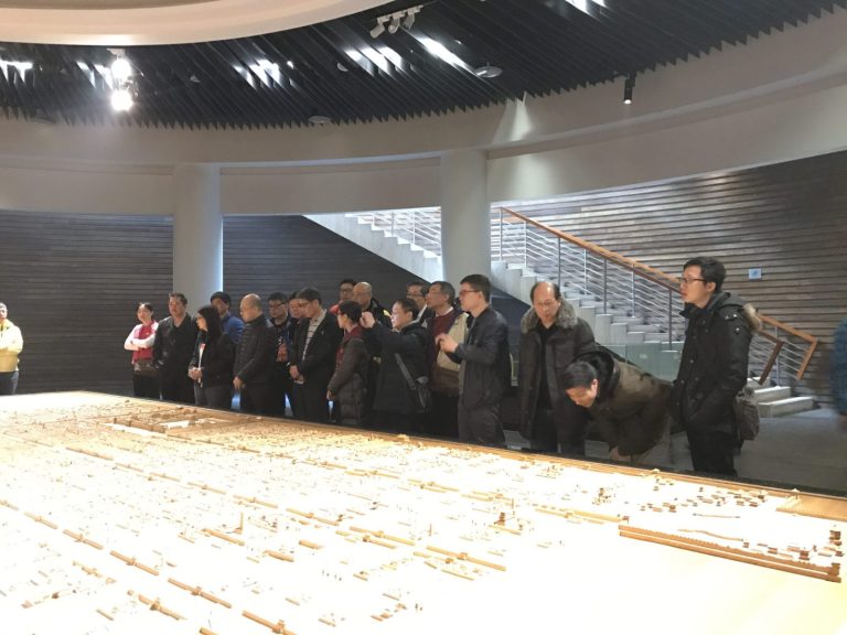 Group viewing architectural model in modern building with staircase and slatted walls.