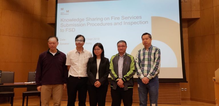 Five people posing in front of a presentation screen about fire services submission procedures.