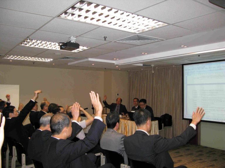 Audience members raising hands during a business presentation in a conference room.