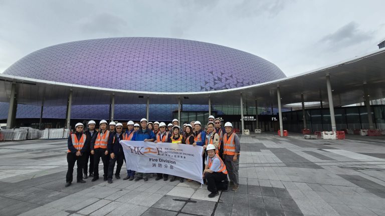 Group of engineers in hard hats holding banner outside Hong Kong Stadium.